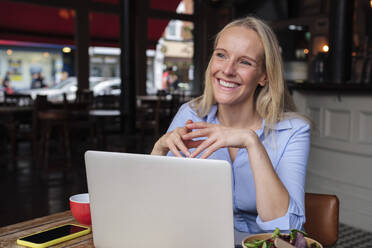 Lächelnder Freiberufler sitzt mit Laptop und Salat auf dem Tisch in einem Café - ASGF04699