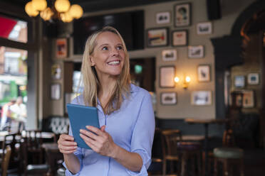 Smiling businesswoman holding tablet PC in pub - ASGF04708