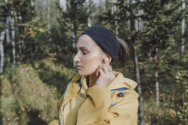 Woman listening to music through wireless in-ear headphones at forest - VBUF00503