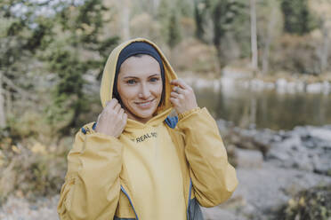 Smiling woman wearing hooded shirt in forest - VBUF00507