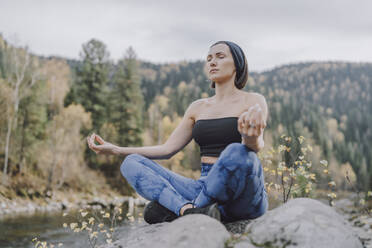 Woman sitting on rock and meditating in forest - VBUF00510