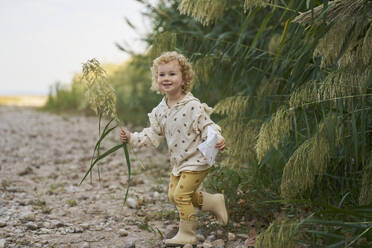 Glückliches Mädchen hält Zweig und läuft in der Nähe von Pflanzen - ANNF00601