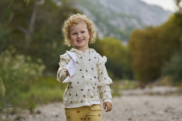 Happy curly haired girl holding paper boat - ANNF00604