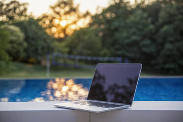 Laptop kept on poolside at sunset - MAMF02896