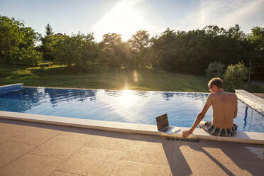 Freelancer sitzt mit Laptop am Pool - MAMF02903