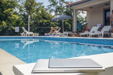 Laptop and tablet PC kept near swimming pool on sunny day - MAMF02907