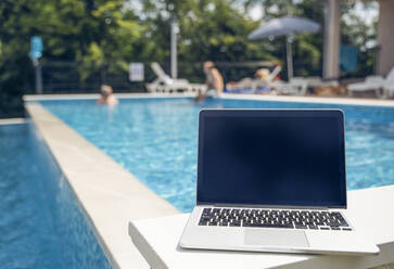 Laptop vor dem Schwimmbad an einem sonnigen Tag - MAMF02909