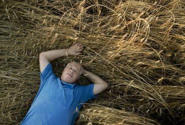 Senior man lying in wheat field - MBLF00123