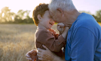 Happy grandfather embracing grandson in agricultural field - MBLF00133