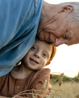 Liebevoller Großvater umarmt Enkel in der Nähe von Nutzpflanzen - MBLF00140
