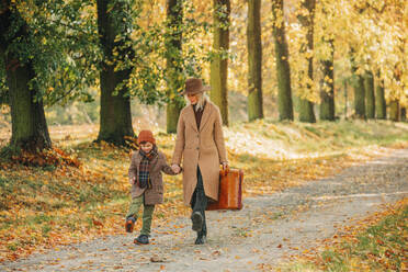 Mother holding hands with son and walking in autumn park - VSNF01418