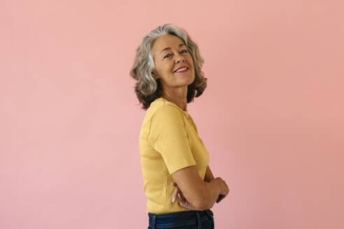 Smiling woman standing with arms crossed against pink background - EBSF04020