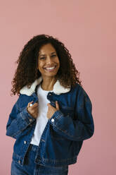 Lächelnde Frau in Jeansjacke vor einem rosa Hintergrund - EBSF04021