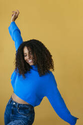 Smiling woman wearing blue sweater and dancing against yellow background - EBSF04037