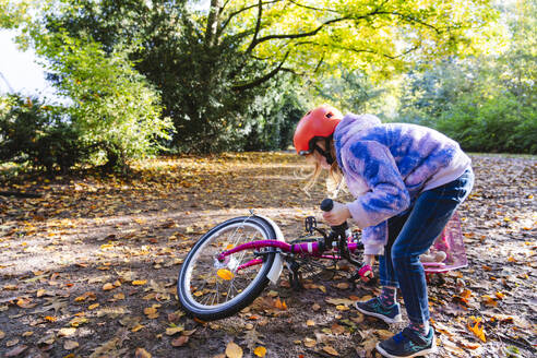 Mädchen hebt im Park ein heruntergefallenes Fahrrad vom Boden auf - IHF01826