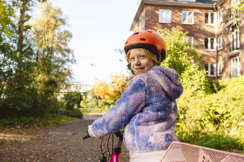 Lächelndes Mädchen mit Fahrrad im Park, das über die Schulter schaut - IHF01828