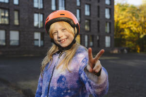 Lächelndes Mädchen mit Helm, das mit der Hand ein Friedenszeichen macht - IHF01832