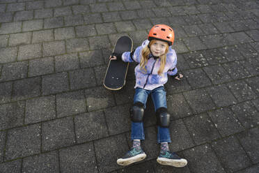 Mädchen sitzt neben dem Skateboard auf dem Boden - IHF01840