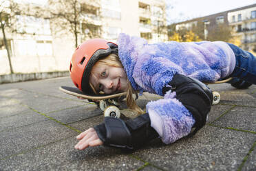 Verspieltes Mädchen über Skateboard auf der Straße liegend - IHF01841