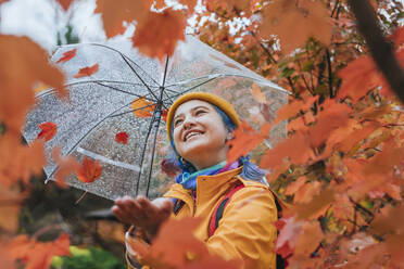 Happy woman with umbrella enjoying rain in autumn park - YTF01367