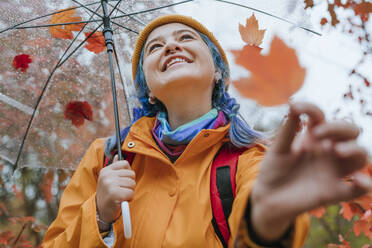 Lächelnde Frau mit Regenschirm und Blatt im herbstlichen Park - YTF01370