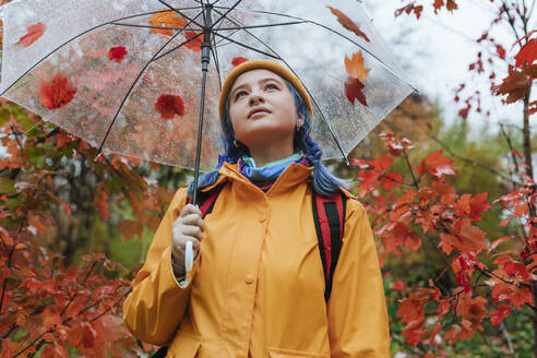 Contemplative woman holding umbrella in autumn park - YTF01371