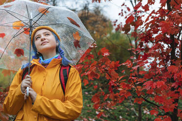 Glückliche Frau hält Regenschirm in der Nähe von Baum im Herbst Park - YTF01373