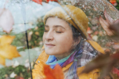 Smiling woman wearing knit hat seen through umbrella - YTF01374