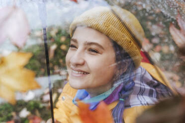 Happy woman wearing knit hat seen through umbrella - YTF01375