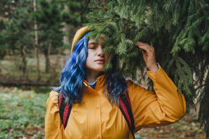 Woman wearing jacket and touching branches of tree in forest - YTF01398