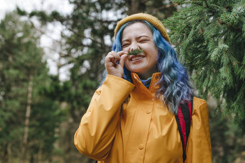 Happy woman smelling twig in forest - YTF01404