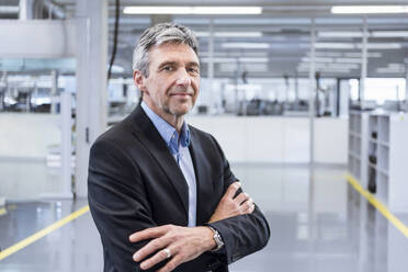 Smiling businessman with arms crossed in factory - DIGF20975