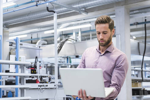 Junger Ingenieur arbeitet in einer Fabrik an einem Laptop - DIGF20978