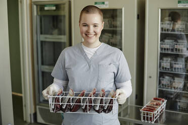 Lächelnder Labortechniker mit einem Regal voller Blutbeutel in einer Klinik - KPEF00295