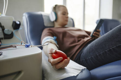 Hand einer Frau, die einen weichen Ball hält, der auf einer Couch im Blutspendezentrum liegt - KPEF00311