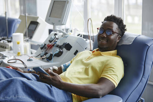 Lächelnder Mann beim Blutspenden auf der Couch liegend - KPEF00316