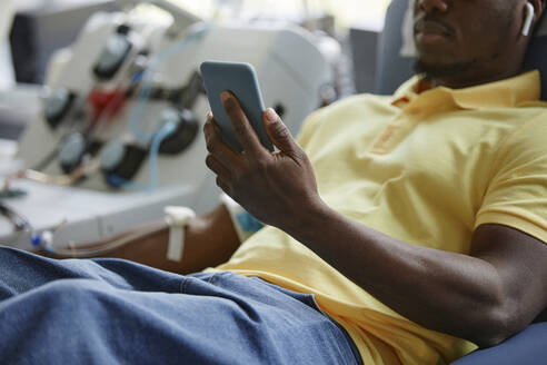 Hand eines Mannes, der ein Mobiltelefon in einem Blutspendezentrum hält - KPEF00318