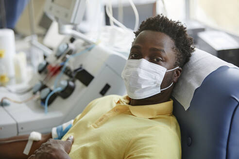 Mann mit Gesichtsschutzmaske liegt auf einer Liege im Blutspendezentrum - KPEF00321