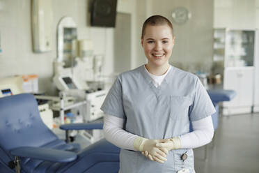 Smiling healthcare worker standing with hands clasped at blood donation center - KPEF00327
