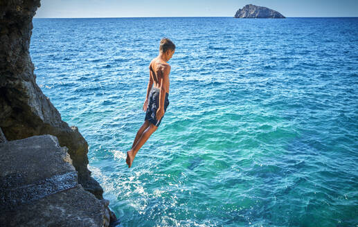 Junge springt von Klippe in blaues Meer - DIKF00771