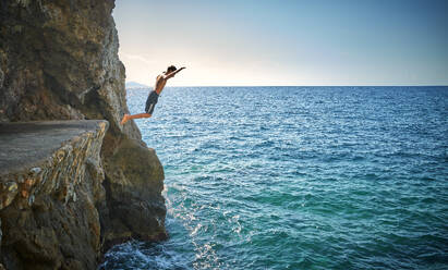 Boy jumping from cliff in sea - DIKF00772