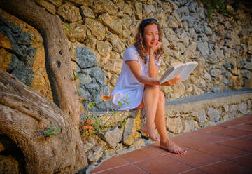 Frau liest Buch in der Nähe einer Steinmauer - DIKF00779