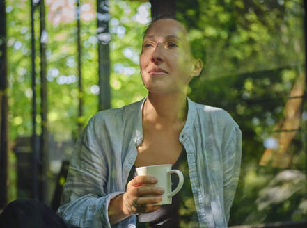 Woman with cup in hand looking through window - DIKF00781