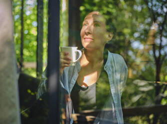 Reife Frau genießt eine Tasse Kaffee und schaut durch das Fenster - DIKF00782