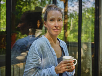 Frau mit Kaffeetasse vor einem Fenster - DIKF00784