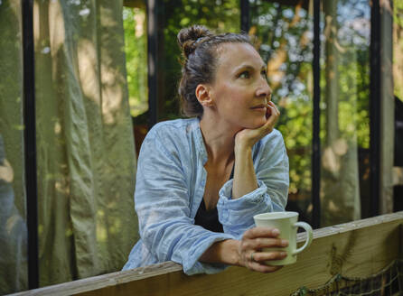 Thoughtful mature woman enjoying coffee on porch - DIKF00787