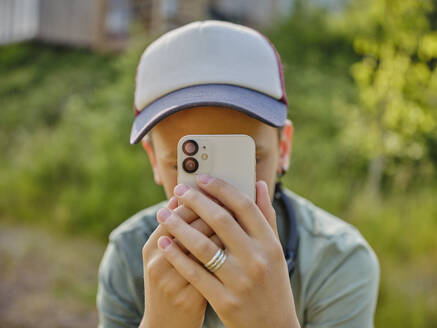 Boy taking picture with smart phone at forest - DIKF00789