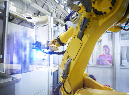 Technician operating yellow robotic arm through tablet PC in factory - CVF02684