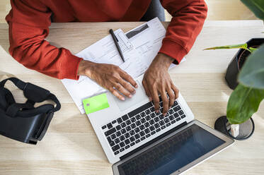 Freiberufler, der an einem Laptop arbeitet und Dokumente am Schreibtisch im Büro zu Hause durchgeht - ALKF00812