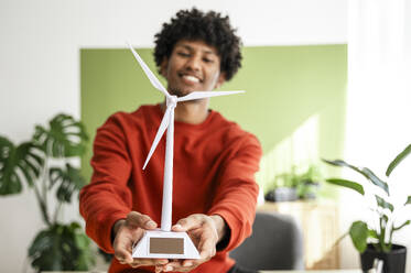 Young freelancer holding wind turbine model at home office - ALKF00822